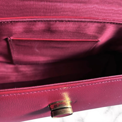 Close-up of the interior of a red  leather handbag, showing a satin-lined pocket and a gold-tone metal snap closure.