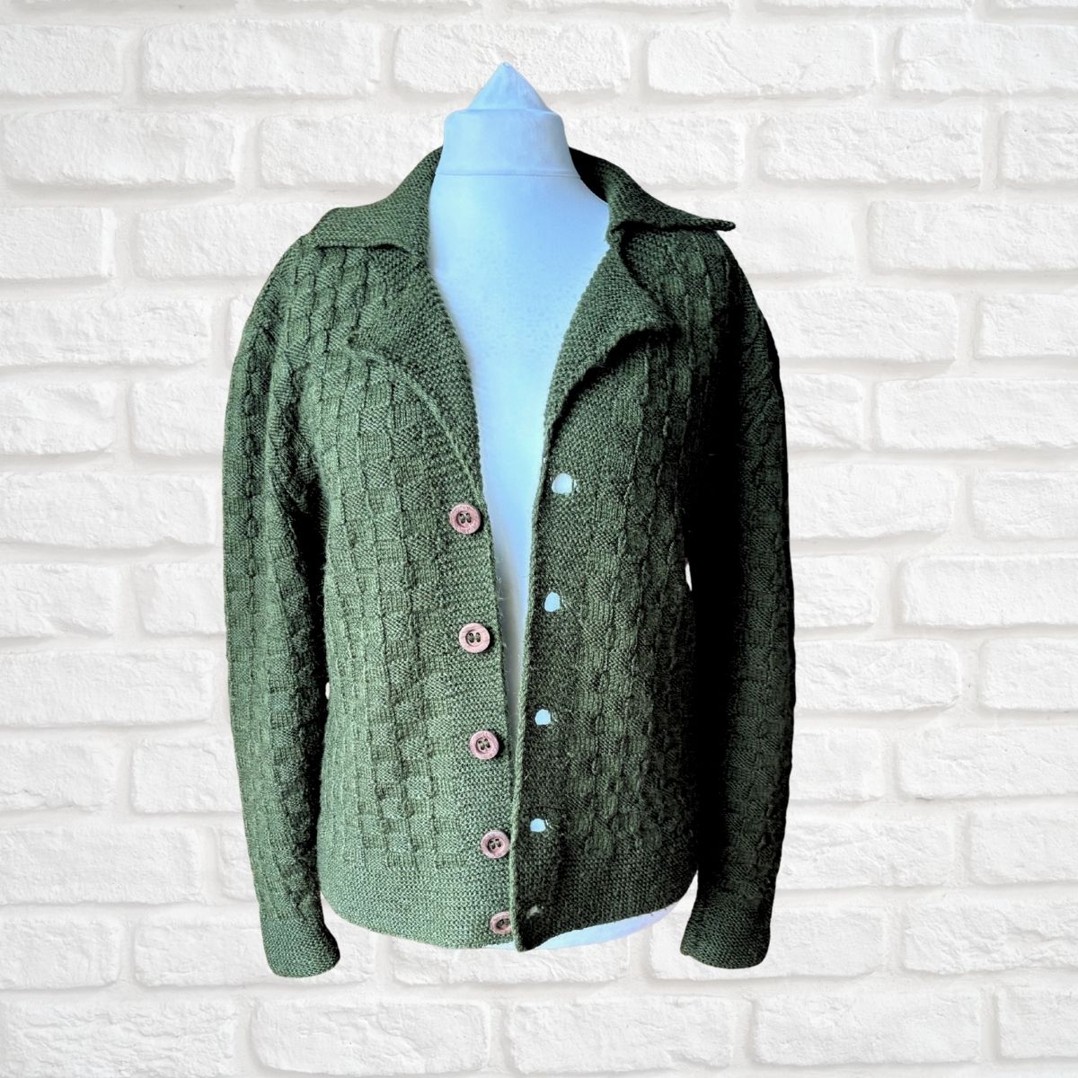 A green textured knit cardigan sweater displayed on a light blue mannequin torso against a white brick wall background.