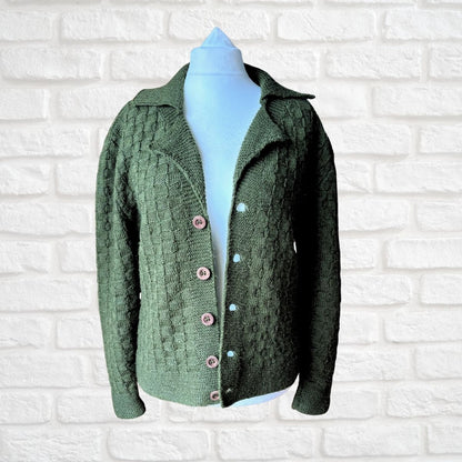 A green textured knit cardigan sweater displayed on a light blue mannequin torso against a white brick wall background.