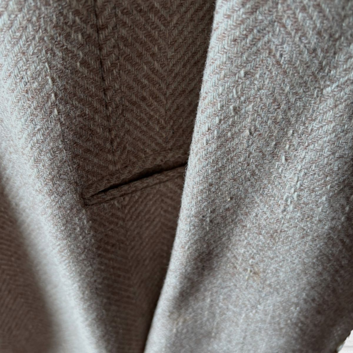 Close-up of a herringbone patterned jacket  in a warm taupe-beige colour, showing the woven texture and fold details.