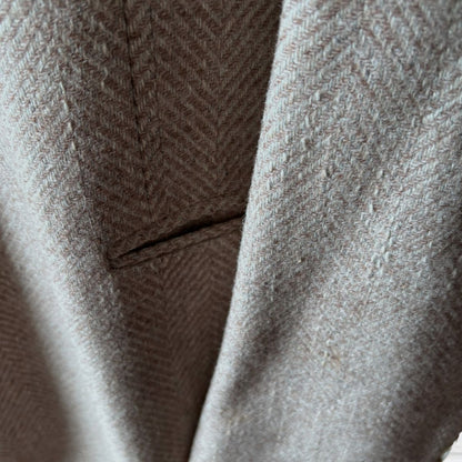 Close-up of a herringbone patterned jacket  in a warm taupe-beige colour, showing the woven texture and fold details.