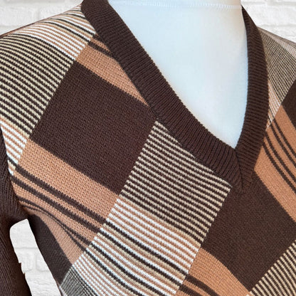 A close-up of a knit V-neck sweater displayed on a white mannequin torso. The sweater features a patchwork design with large brown blocks, tan blocks, and narrow horizontal stripes in white and gray.