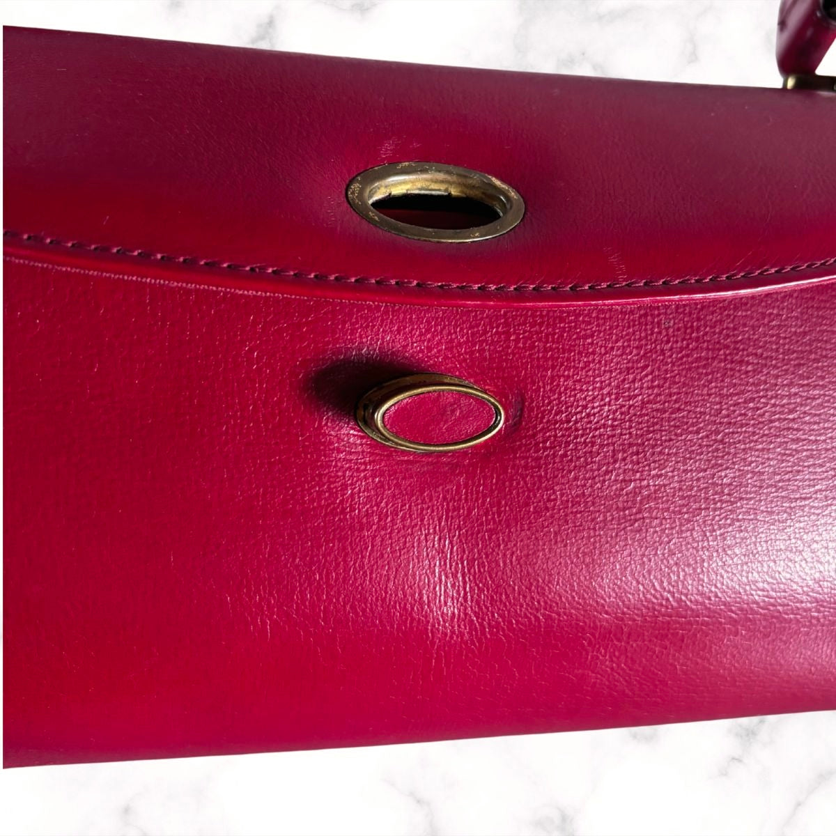 Close-up of a red textured leather handbag showing a metal ring detail and stitching on a white marble surface.
