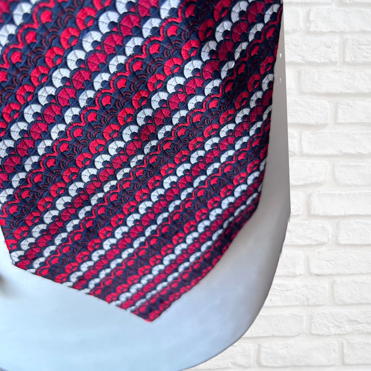 Close-up of a patterned tie with red, white, and blue design on a white brick wall background.