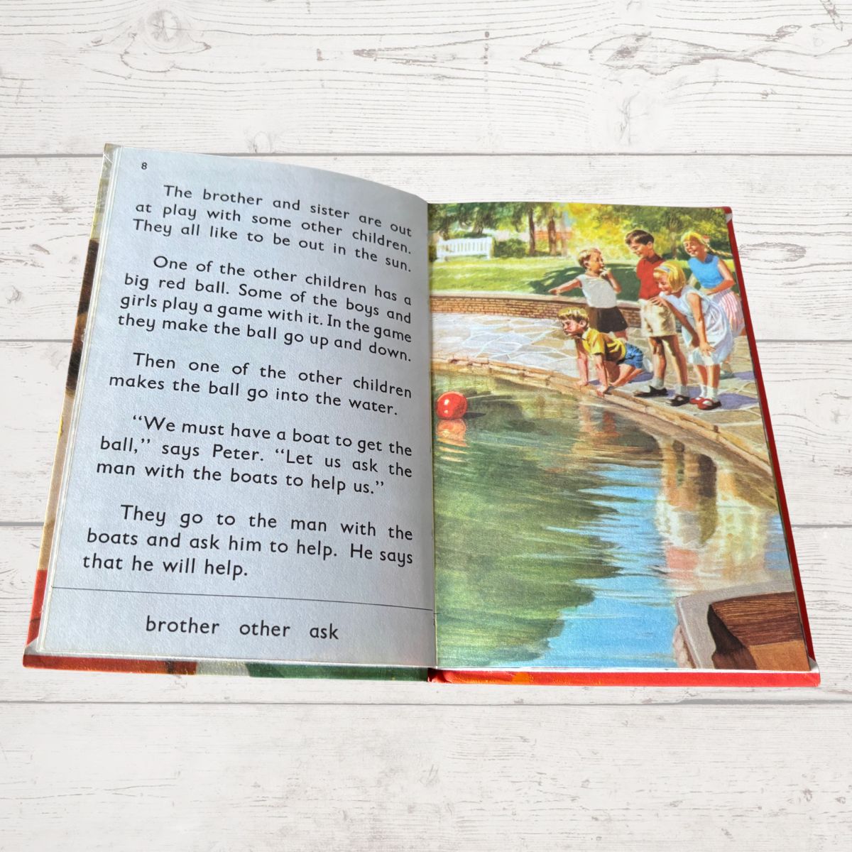 Open book with text and illustration of children by a pond on a wooden surface