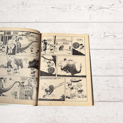 Open comic book with black and white illustrations on a light wooden surface