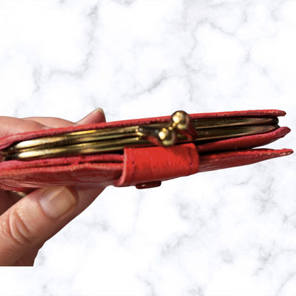Red wallet with gold accents held by a hand against a white background