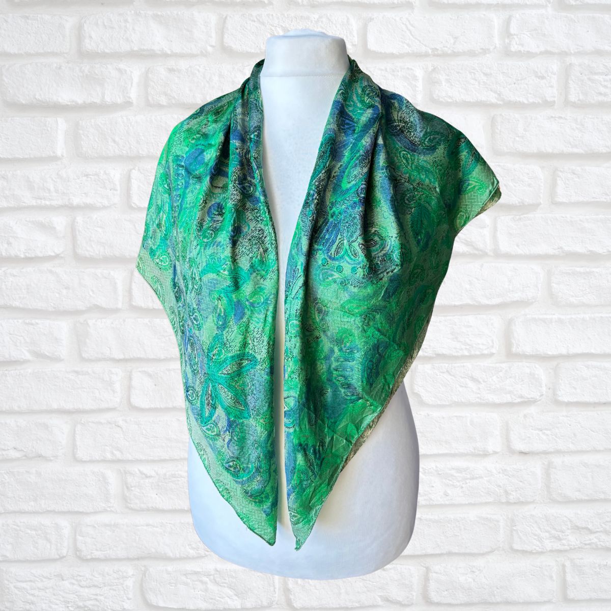 Green patterned scarf on a mannequin against a white brick wall background