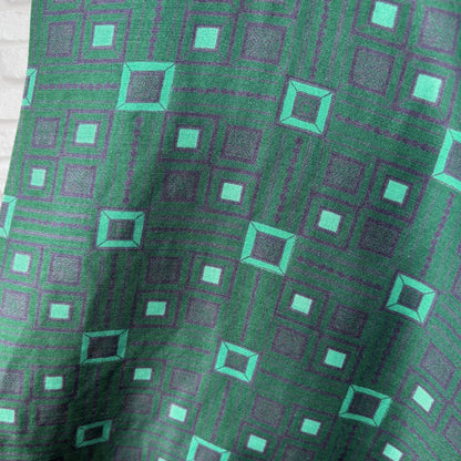 A close-up of a green patterned fabric with a geometric design of teal and purple squares.