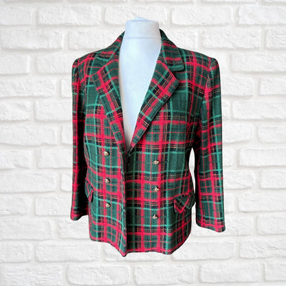 A double-breasted plaid blazer in green, red, and black tartan, displayed on a white mannequin torso against a white brick wall background.