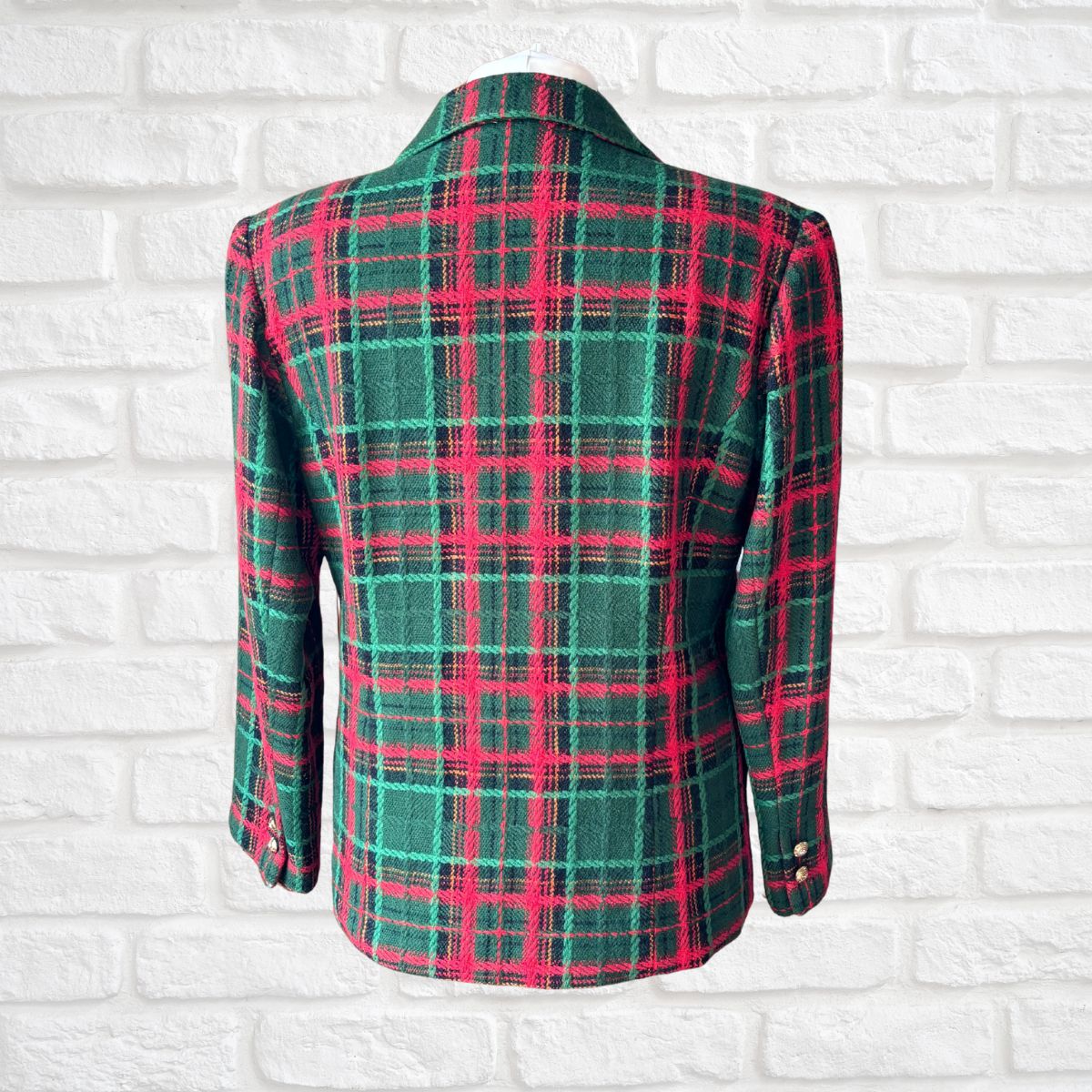 A green and red plaid blazer jacket displayed on a white brick wall background.
