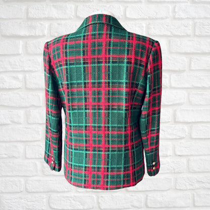 A green and red plaid blazer jacket displayed on a white brick wall background.