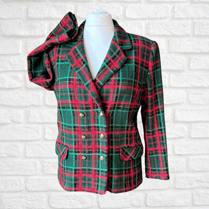 A women's double-breasted plaid blazer jacket in green and red tartan, displayed on a white mannequin torso against a white brick wall background.