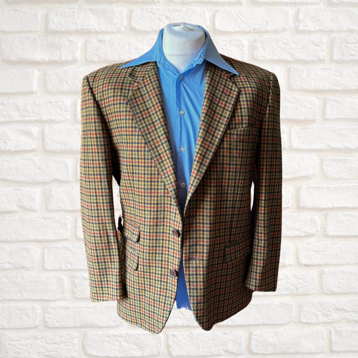 Plaid blazer over a blue shirt on a mannequin against a white brick wall.