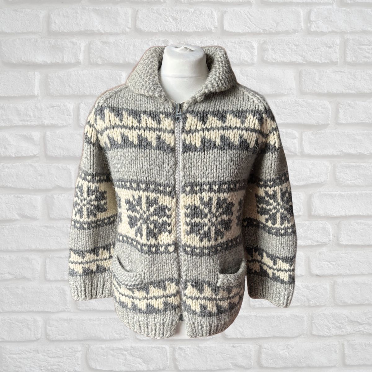 Knitted sweater with a zig zag pattern on a mannequin against a white brick wall.