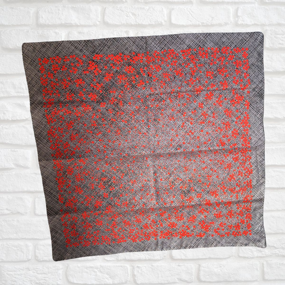 Gray scarf with red floral pattern on a white brick wall background