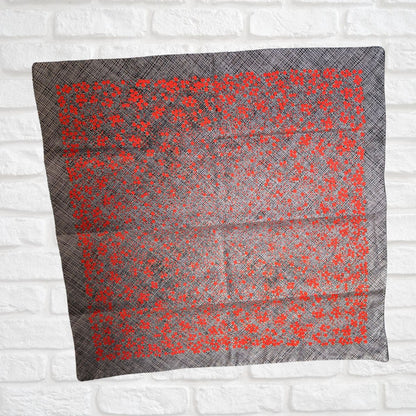 Gray scarf with red floral pattern on a white brick wall background
