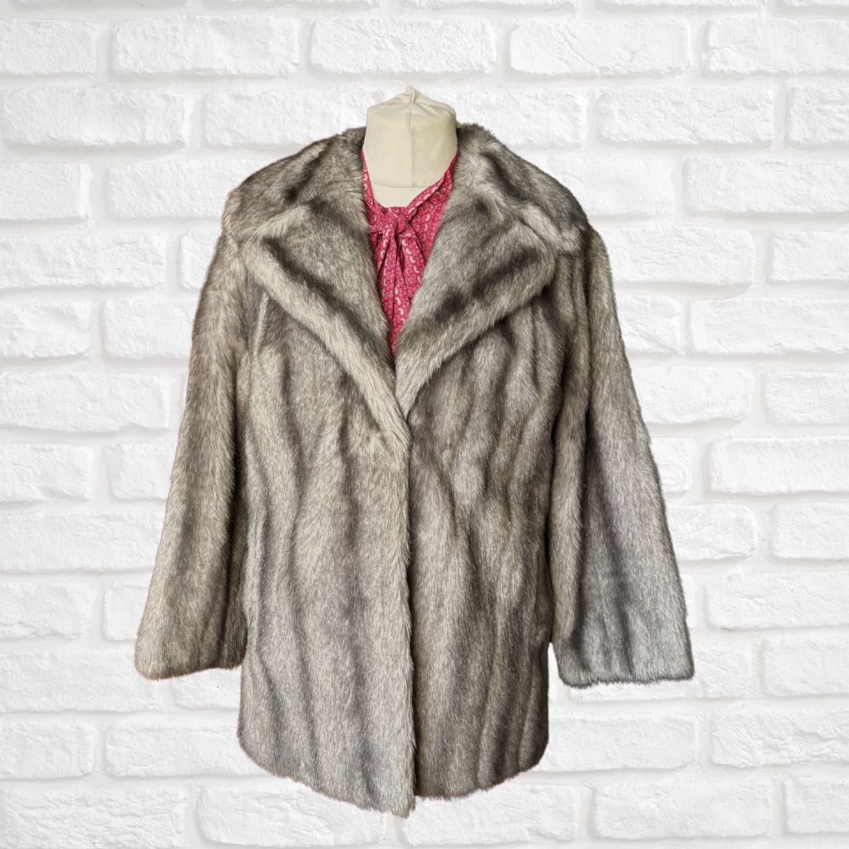 Gray fur coat on a mannequin against a white brick wall background