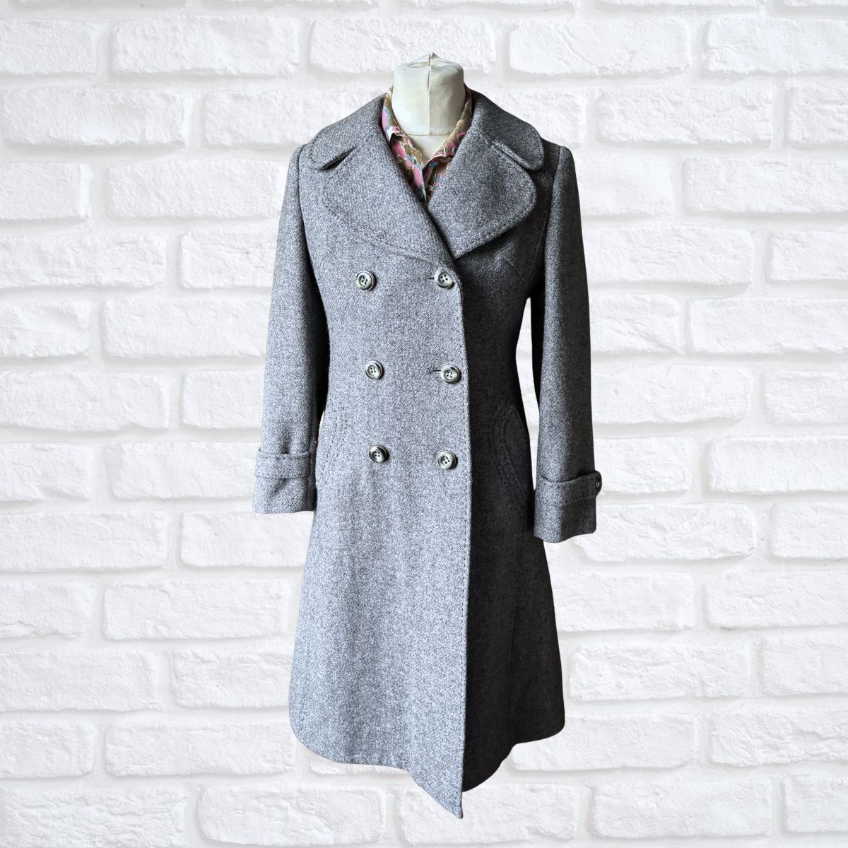 Grey coat on a mannequin against a white brick wall background