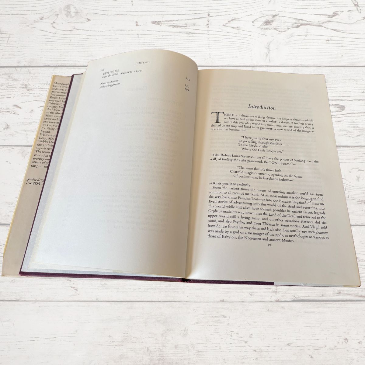 An open book lying flat on a white-painted wooden surface, showing blank interior pages on the left and an introduction page on the right.