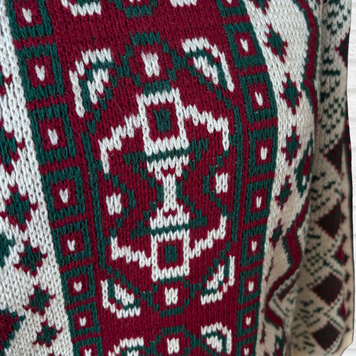 Close-up of a knitted sweater or textile with a geometric pattern in deep red, dark green, and off-white.
