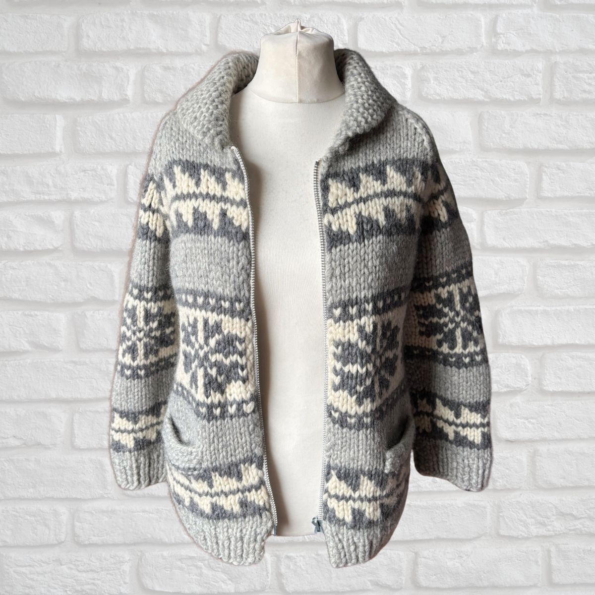 Knitted cardigan with a pattern on a mannequin against a white brick wall.