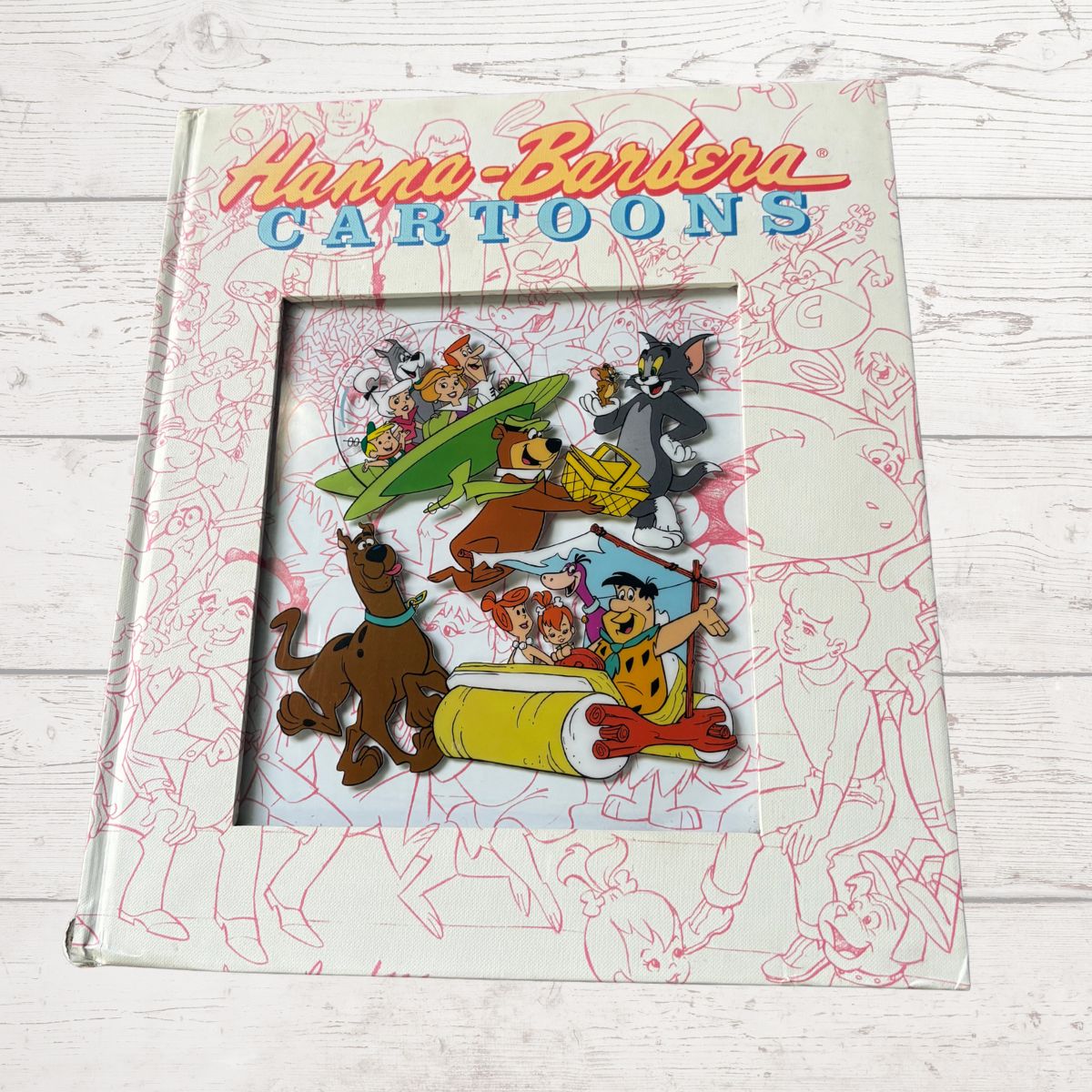 Book titled 'Hanna-Barbera Cartoons' with illustrations of classic cartoon characters on a wooden surface.