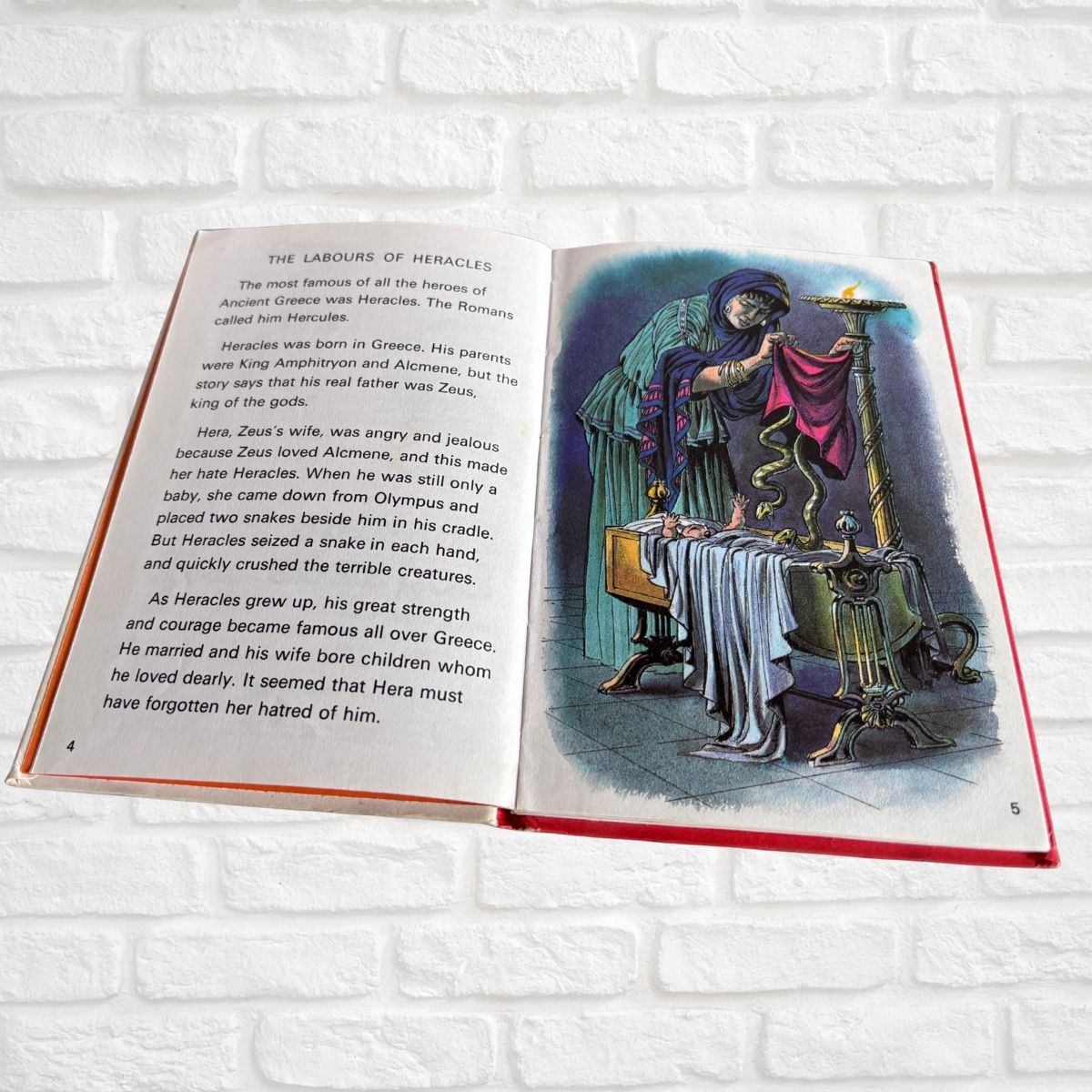 An open hardcover children's book showing a printed story page with black text on the left spread and a colorful illustration of a robed figure holding a sword on the right spread, photographed against a white brick wall background.