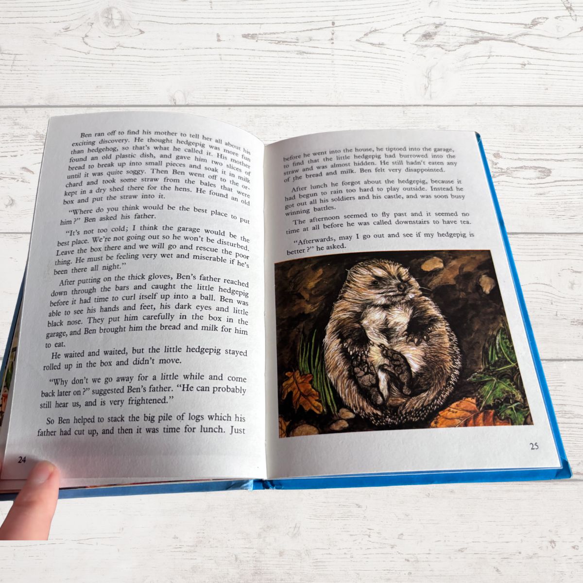 An open children's book with printed text on both pages and a small color photograph showing autumn leaves, held open by a hand on a light wood surface.