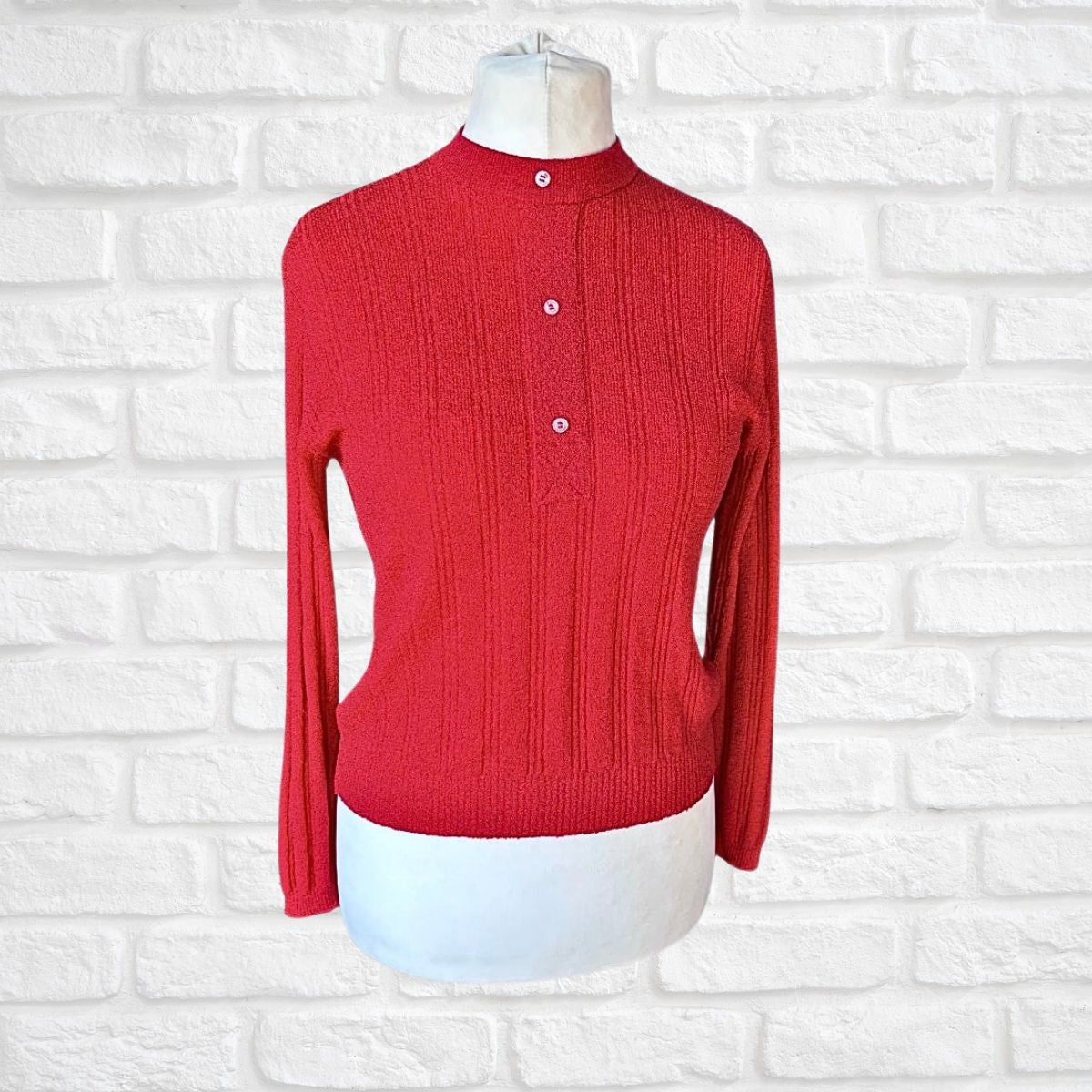 A red ribbed knit mock-neck sweater displayed on a white mannequin torso against a white brick wall background.