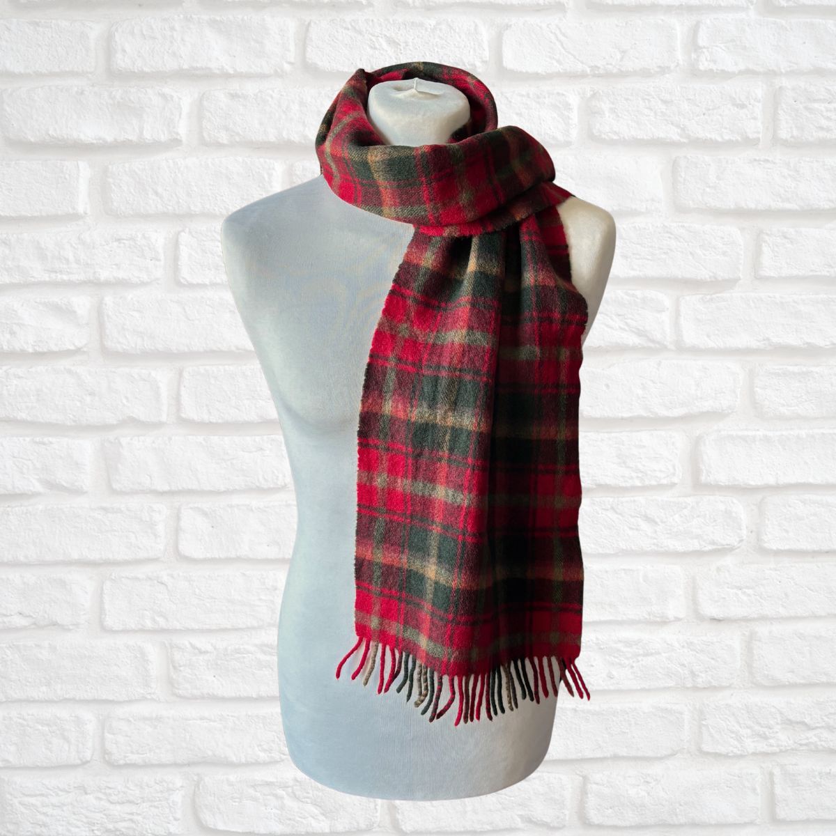 Red and green plaid scarf on a mannequin against a white brick wall.