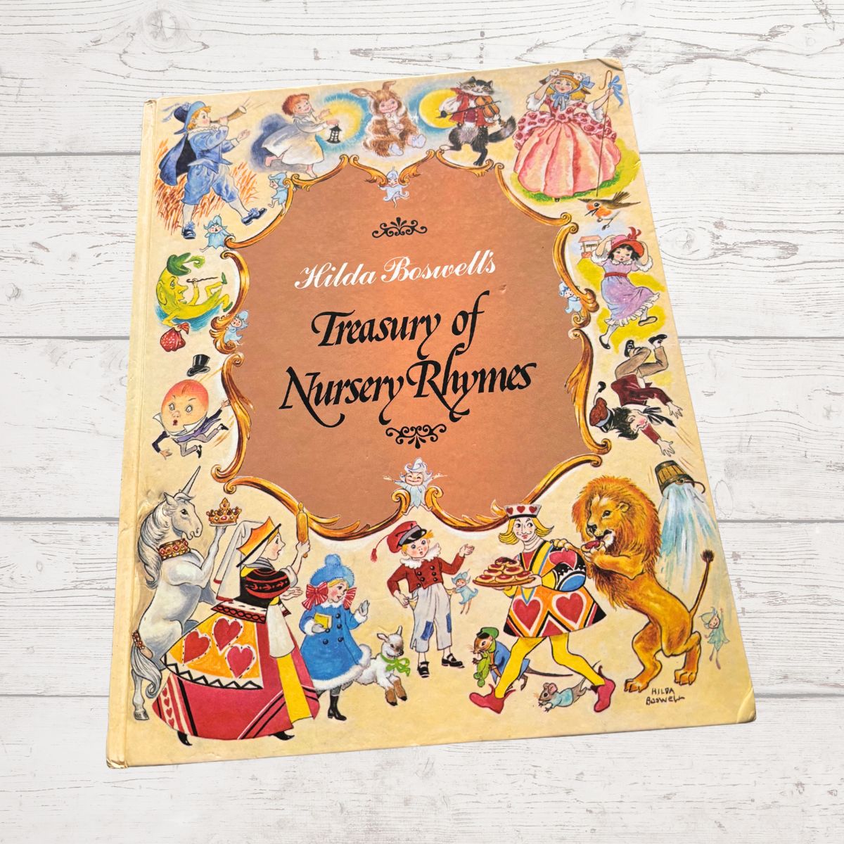 Book titled 'Hilda Boswell's Treasury of Nursery Rhymes' with colorful illustrations on a wooden surface.