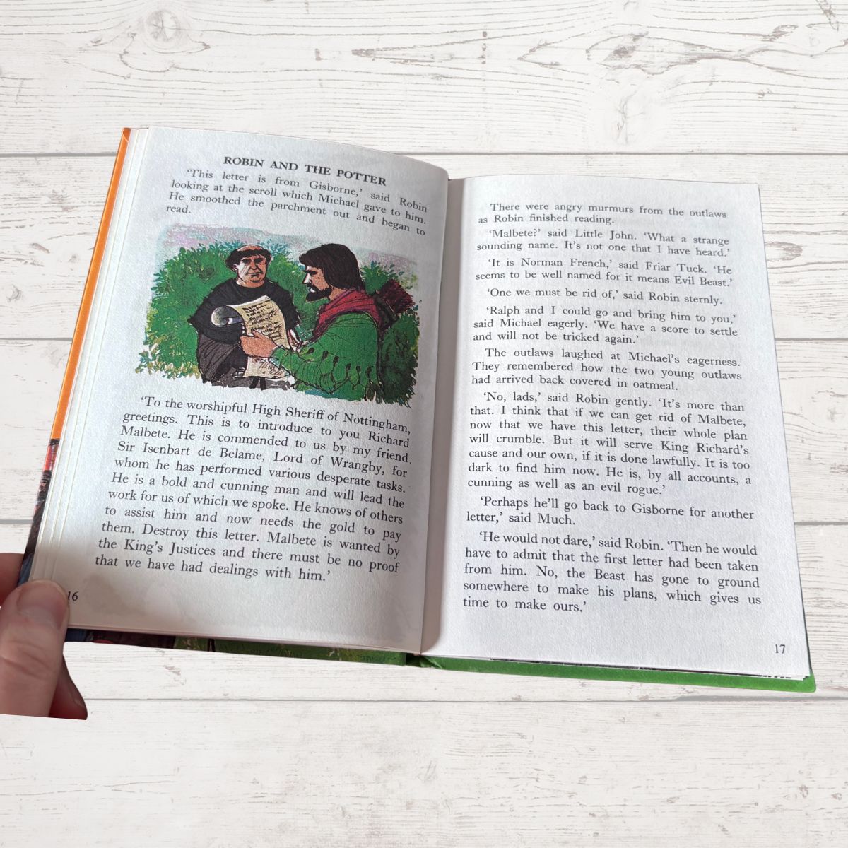 An open book showing printed text pages with an illustrated cover and a green spine, photographed on a light wood surface.