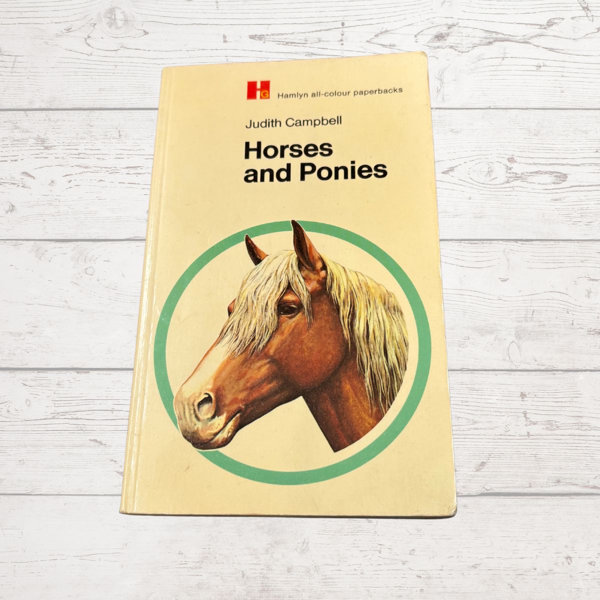 A vintage paperback book titled 'Horses and Ponies' by Judith Campbell, featuring a cream cover with a brown horse illustration, placed on a white wood plank surface.
