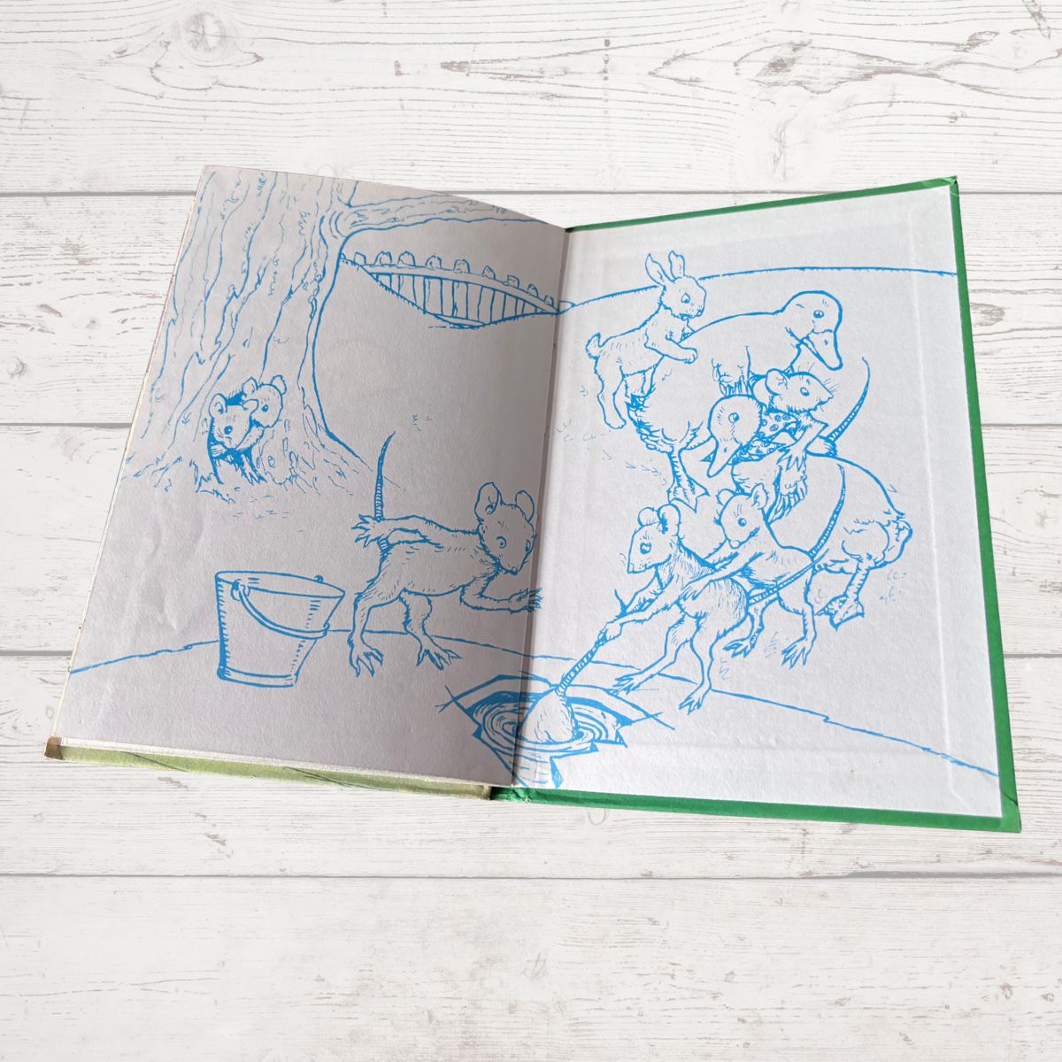 An open vintage children's book with blue ink illustrations of animals and a tree, resting on a white wooden surface.