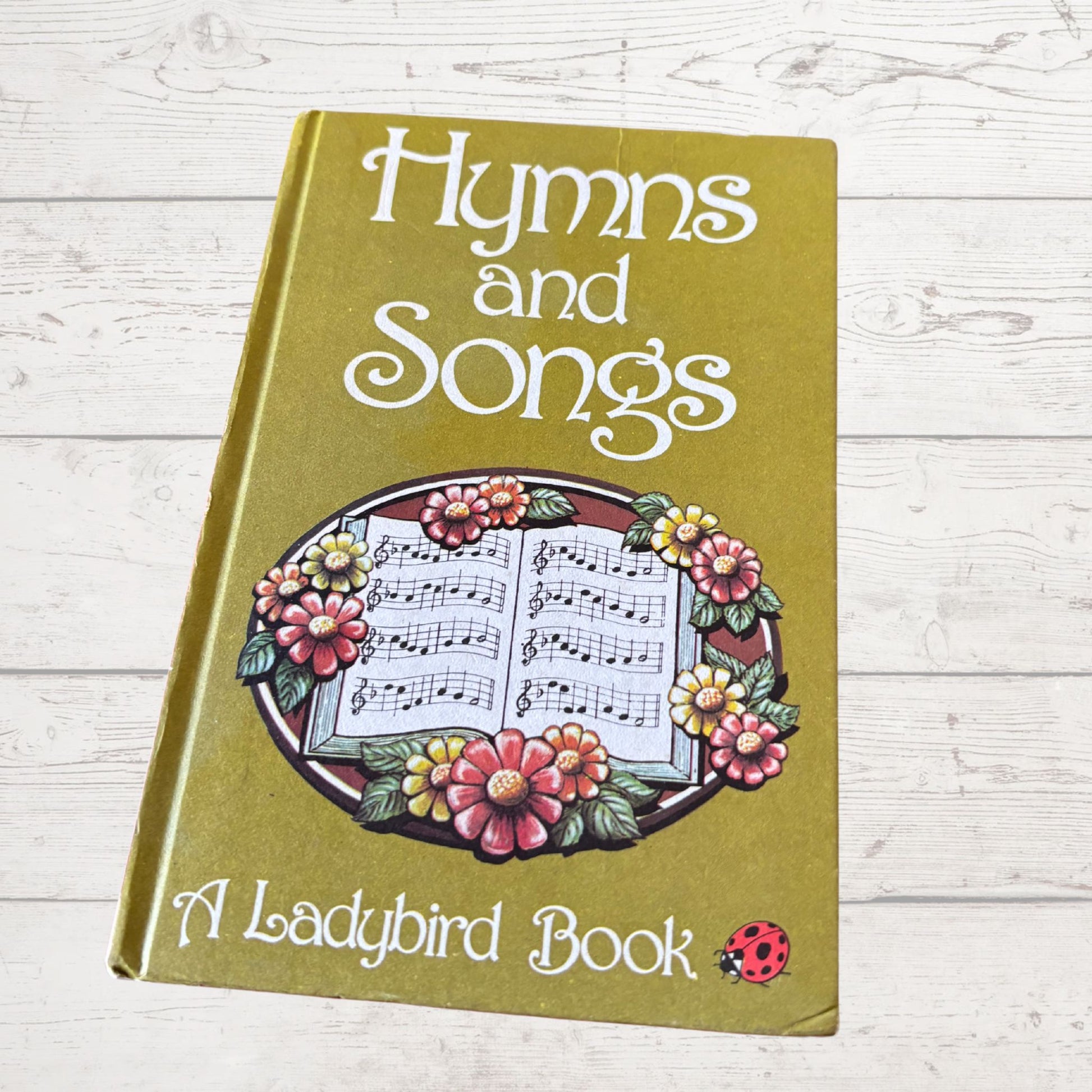 Book titled 'Hymns and Songs' by A Ladybird Book on a wooden surface