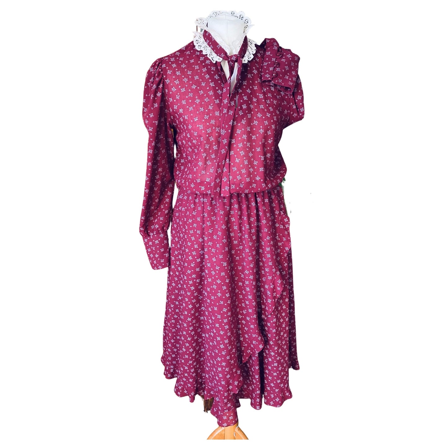 Burgundy prairie dress with pale grey floral print, long deep cuffed sleeves and white frill and tie around the neckline 