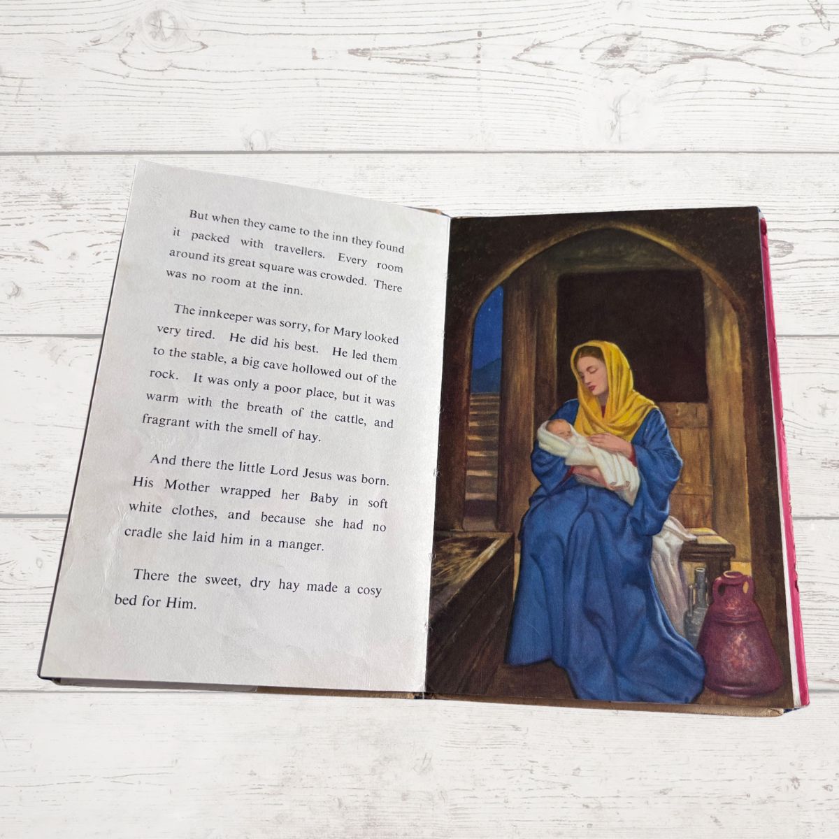 Open book with a illustration of a woman holding a baby in a stable on a wooden surface.