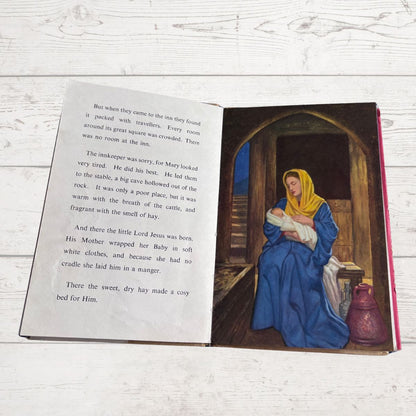 Open book with a illustration of a woman holding a baby in a stable on a wooden surface.