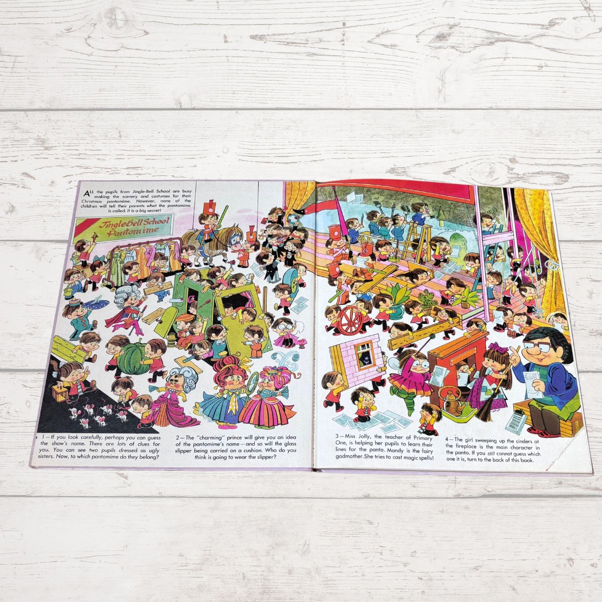An open vintage children's book spread laid flat on a white painted wooden surface, showing colorful cartoon illustrations and printed text.