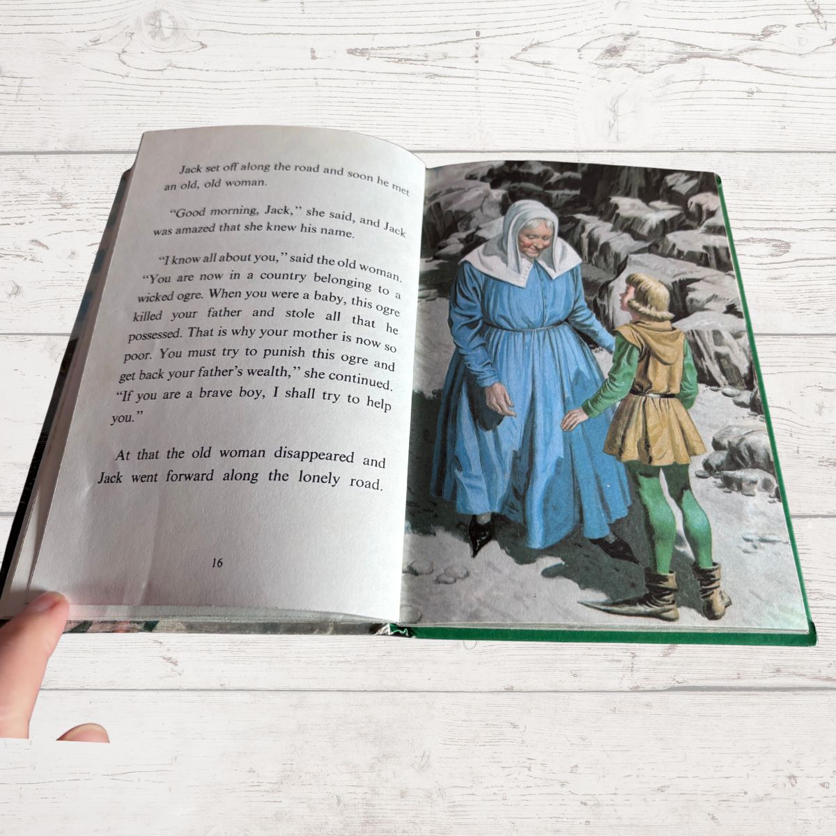 An open children's book lying on a white wood surface, showing printed text on the left page and a vintage-style illustration on the right page.