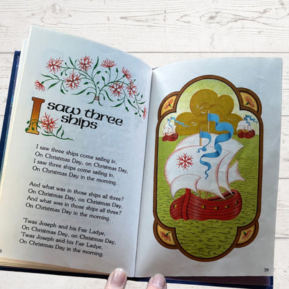 Open book with a Christmas-themed poem and illustration of a ship on a white wooden surface