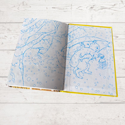 An open children's book with blue line-art illustrations of animals in a snowy scene, displayed on a light gray wood plank surface.