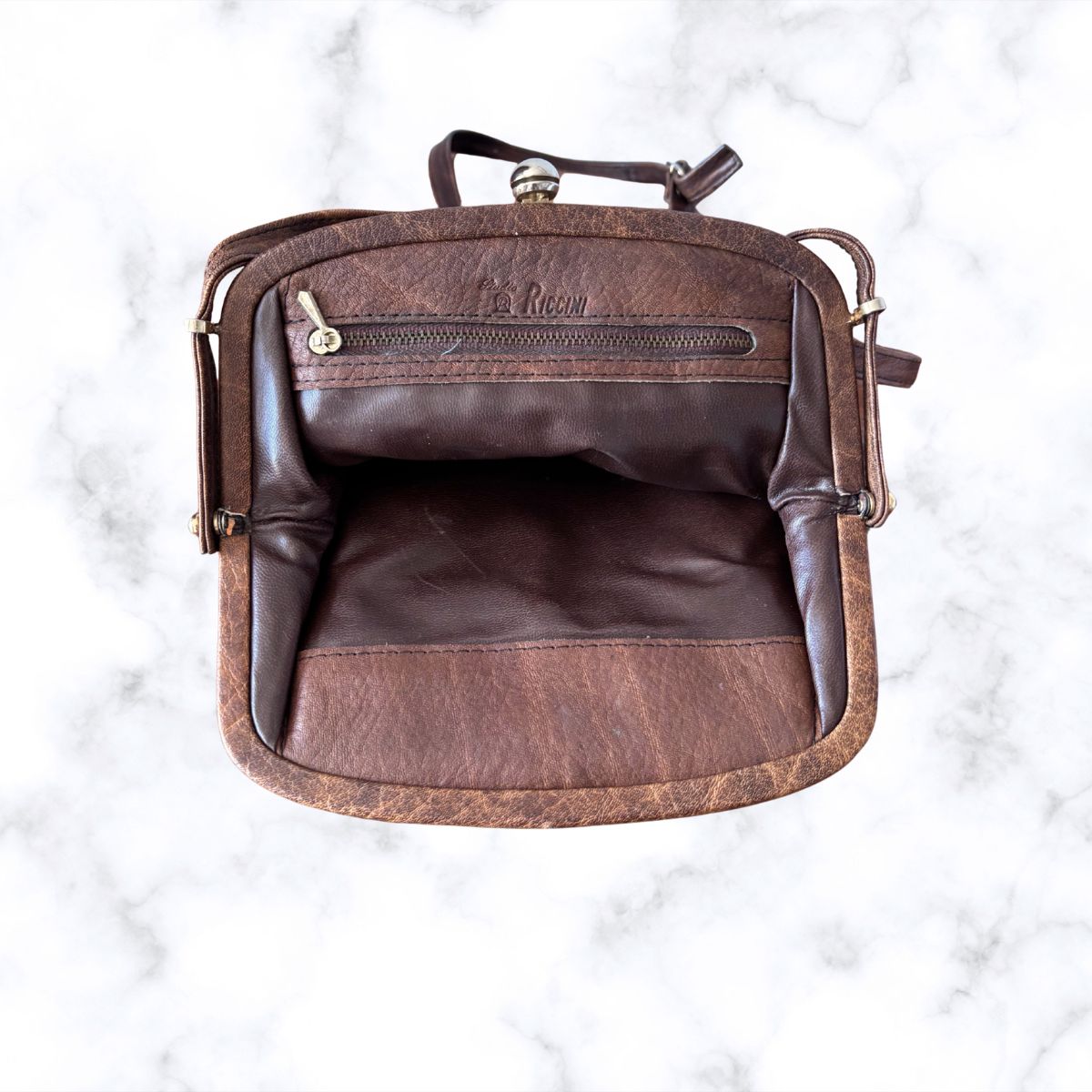 Brown leather look bag with visible branding on a white marble background