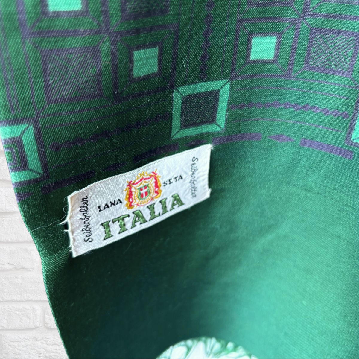 Close-up of a green patterned textile with a sewn white fabric label reading 'LANA SETA  ITALIA' 