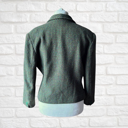 A green and brown textured tweed blazer jacket displayed on a white mannequin torso against a white brick wall background.