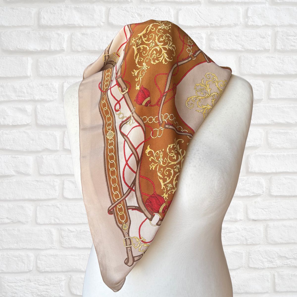 Decorative scarf with intricate patterns on a mannequin against a white brick wall background