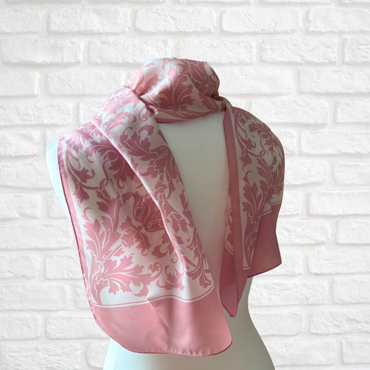 Pink and white patterned scarf on a mannequin against a white brick wall.