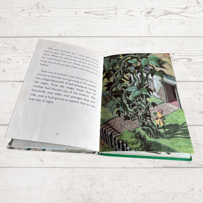 An open children's book lying on a white wood surface, showing a printed story page with text on the left and an illustrated garden scene on the right.