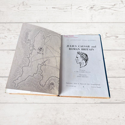 An open vintage book titled 'Julius Caesar and Roman Britain' laid flat on a white wooden surface, showing a map on the left page and the title page with a profile illustration on the right.